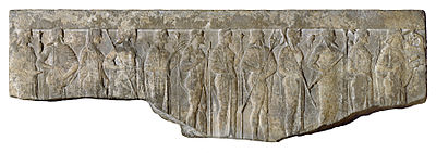 Fragment of a Hellenistic relief (1st century BC – 1st century AD) depicting the Twelve Olympians carrying their attributes in procession; from left to right, Hestia (scepter), Hermes (winged cap and staff), Aphrodite (veiled), Ares (helmet and spear), Demeter (scepter and wheat sheaf), Hephaestus (staff), Hera (scepter), Poseidon (trident), Athena (owl and helmet), Zeus (thunderbolt and staff), Artemis (bow and quiver), Apollo (lyre), from the Walters Art Museum. Courtesy of WikiCommons.