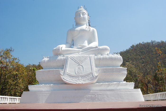 A huge white Buddha near a temple.